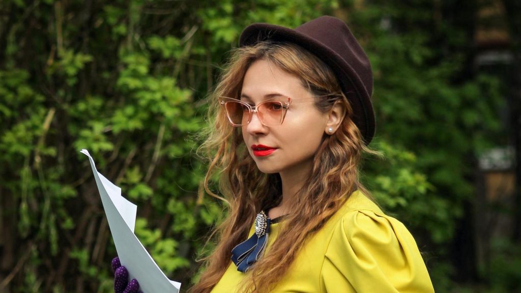 Stylish woman in vintage attire using a typewriter in a scenic outdoor setting.