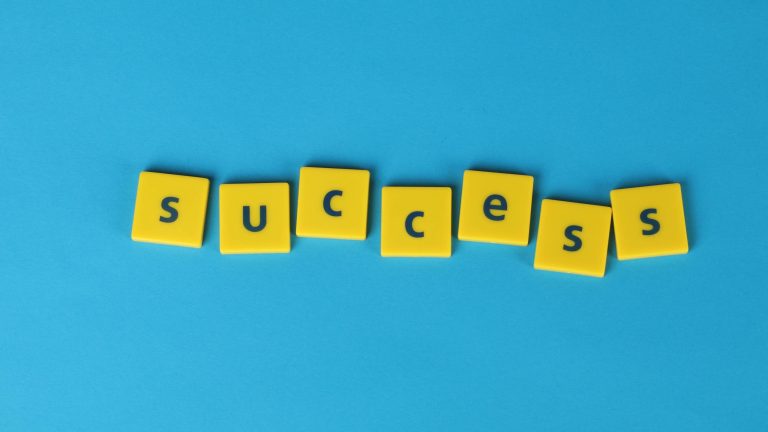Yellow letter tiles spell the word success on a vibrant blue backdrop, symbolizing achievement.